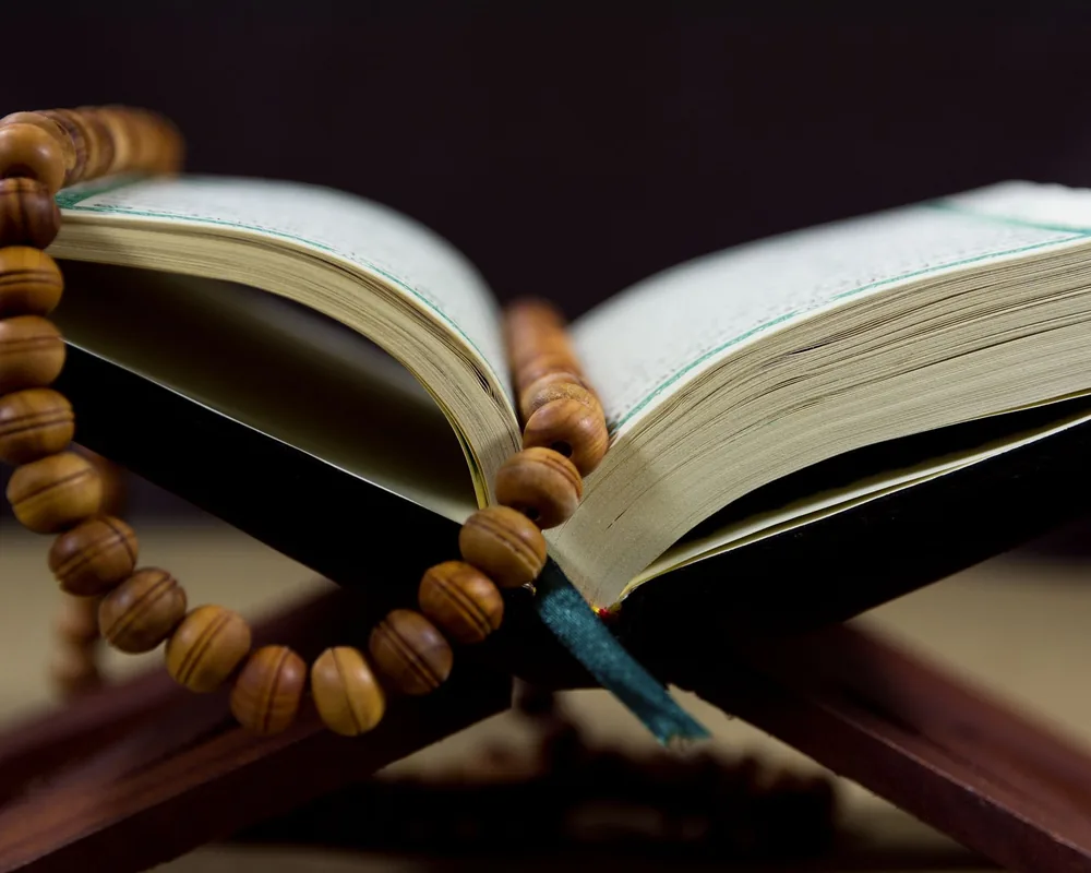 An open book on a wooden rehal with a wooden tasbīḥ draped across it